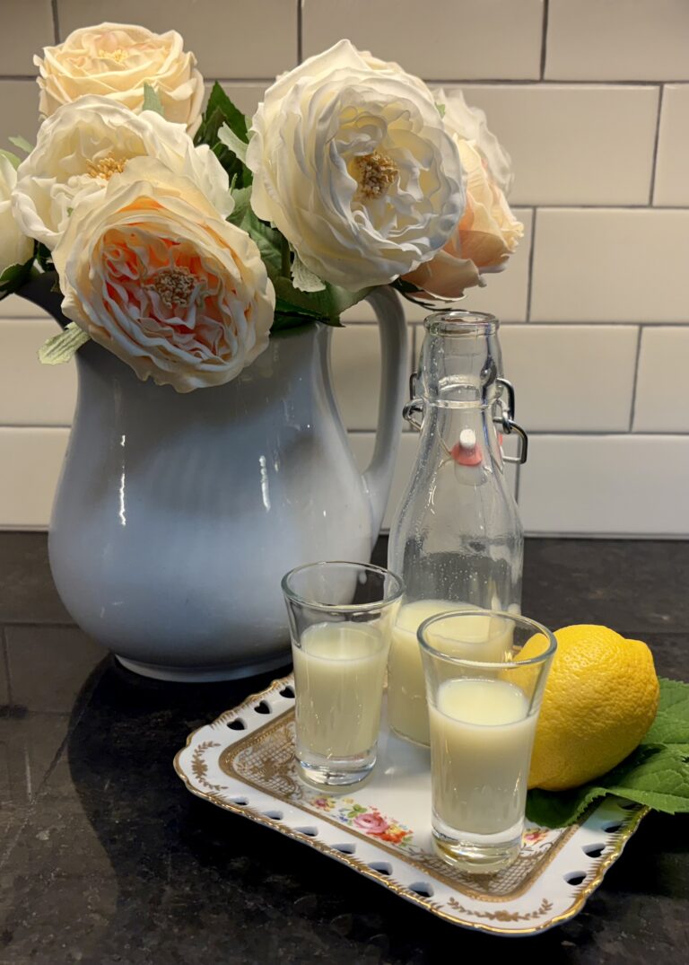a vase of white and yellow flowers with two glasses of a creamy liquid and a lemon